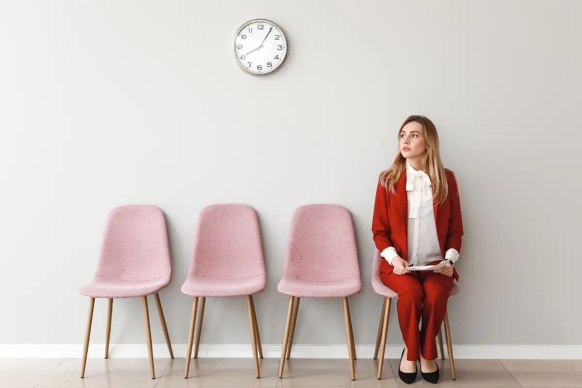 une femme assise sur une chaise avec 3 autres chaises vides à coté d'elle. Elle attend de passer son assessment